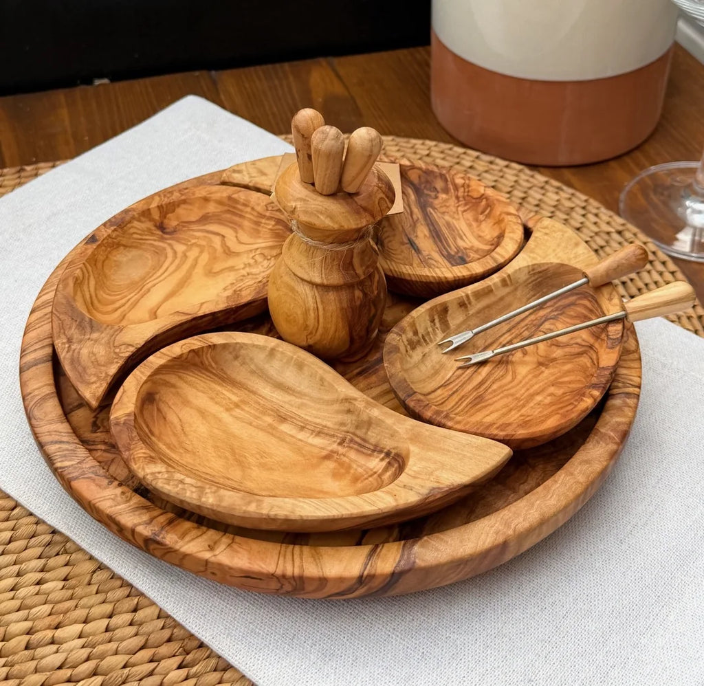 Olive wood appetiser set with serving dishes and metal tongs in a holder on a woven placemat.