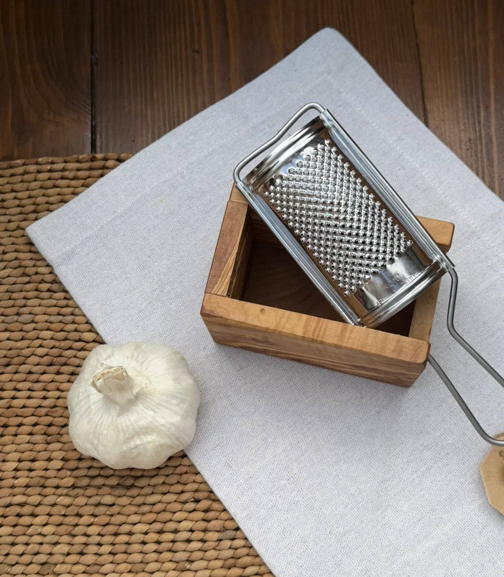 Stainless steel microplane grater set in a natural olive wood box holder with whole garlic bulb.
