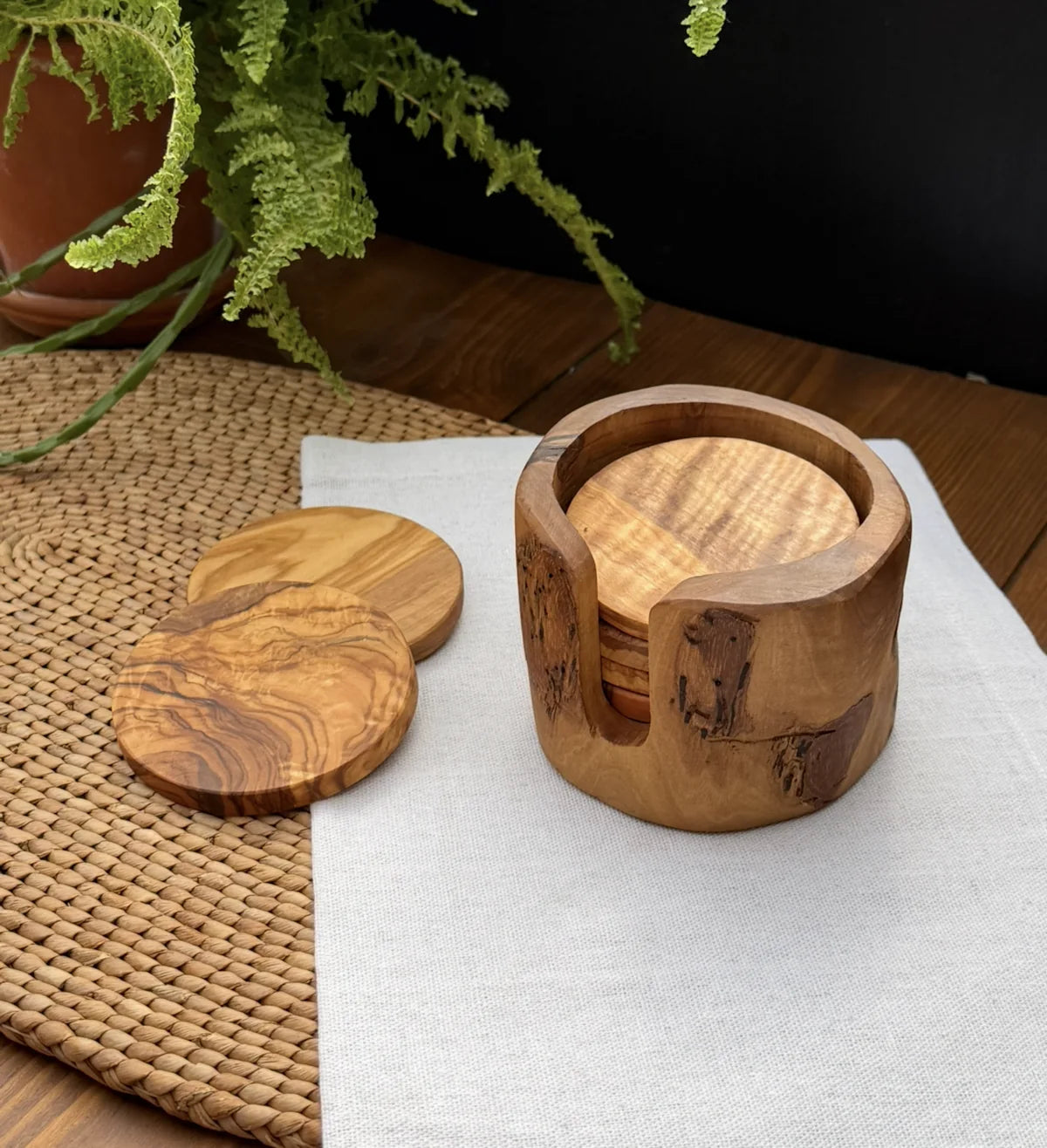 Set of 6 handcrafted olive wood coasters with a matching holder on a white linen cloth.