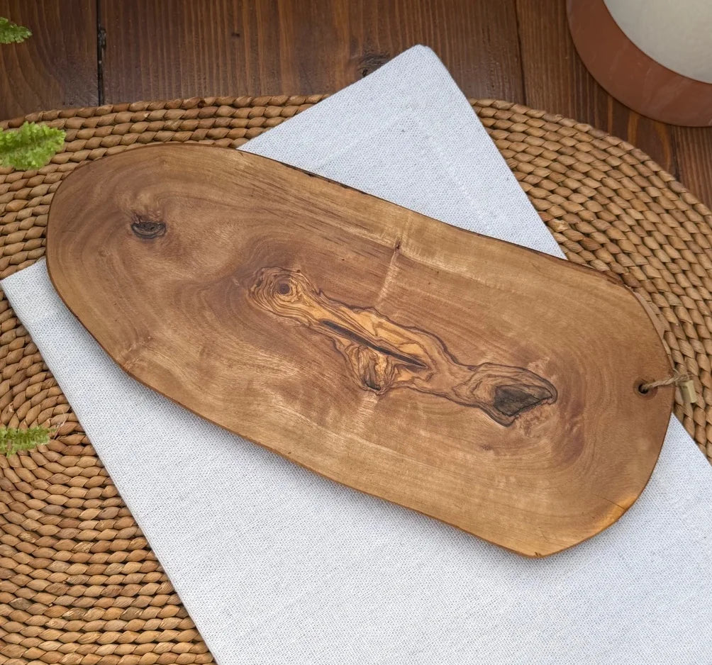 Handcrafted olive wood serving board with a live edge and natural grain knot on a white napkin.