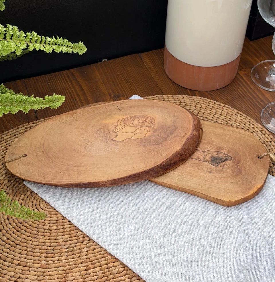 Two olive wood serving boards with natural live edges and engraved details on a woven placemat.
