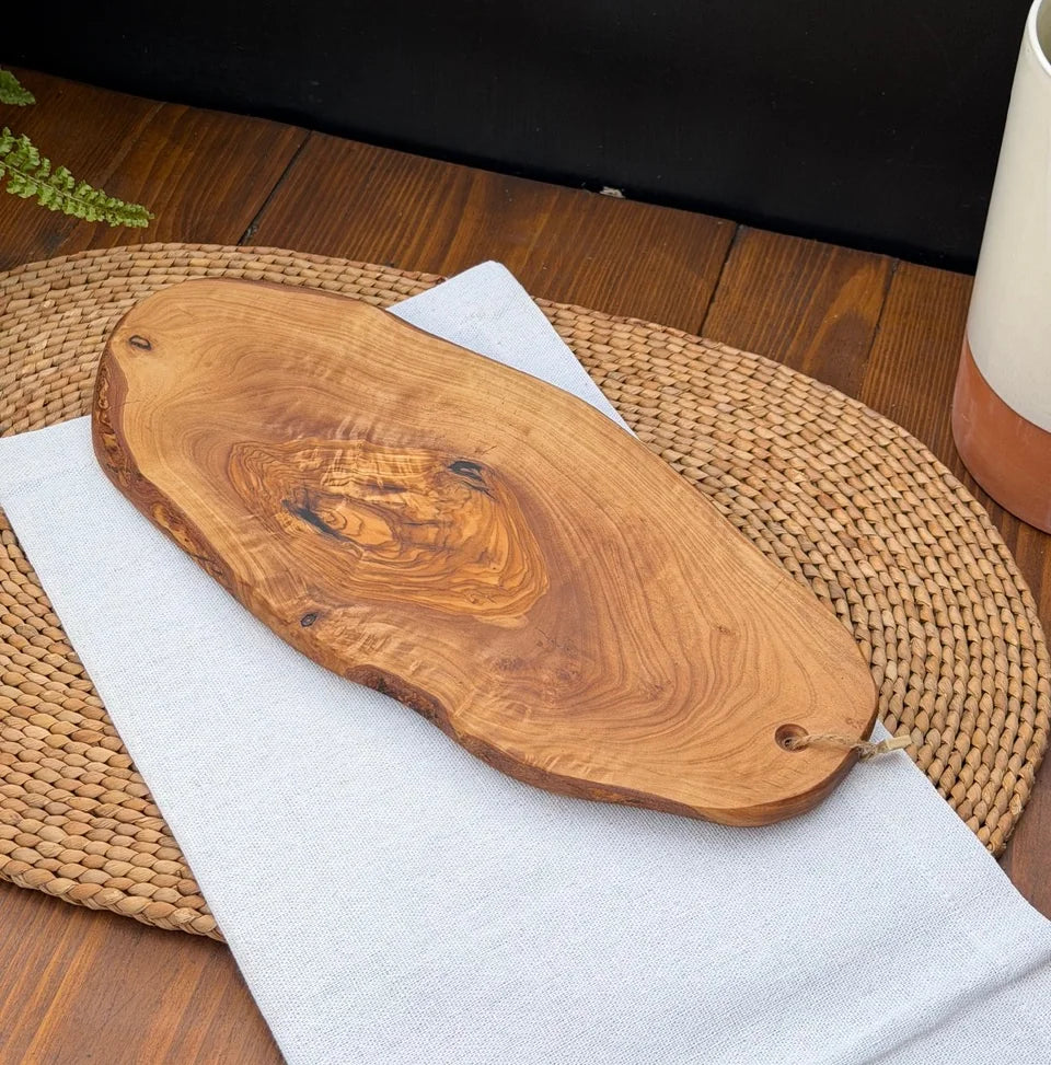 Organic live-edge olive wood serving board resting on a white cloth over a woven placemat.