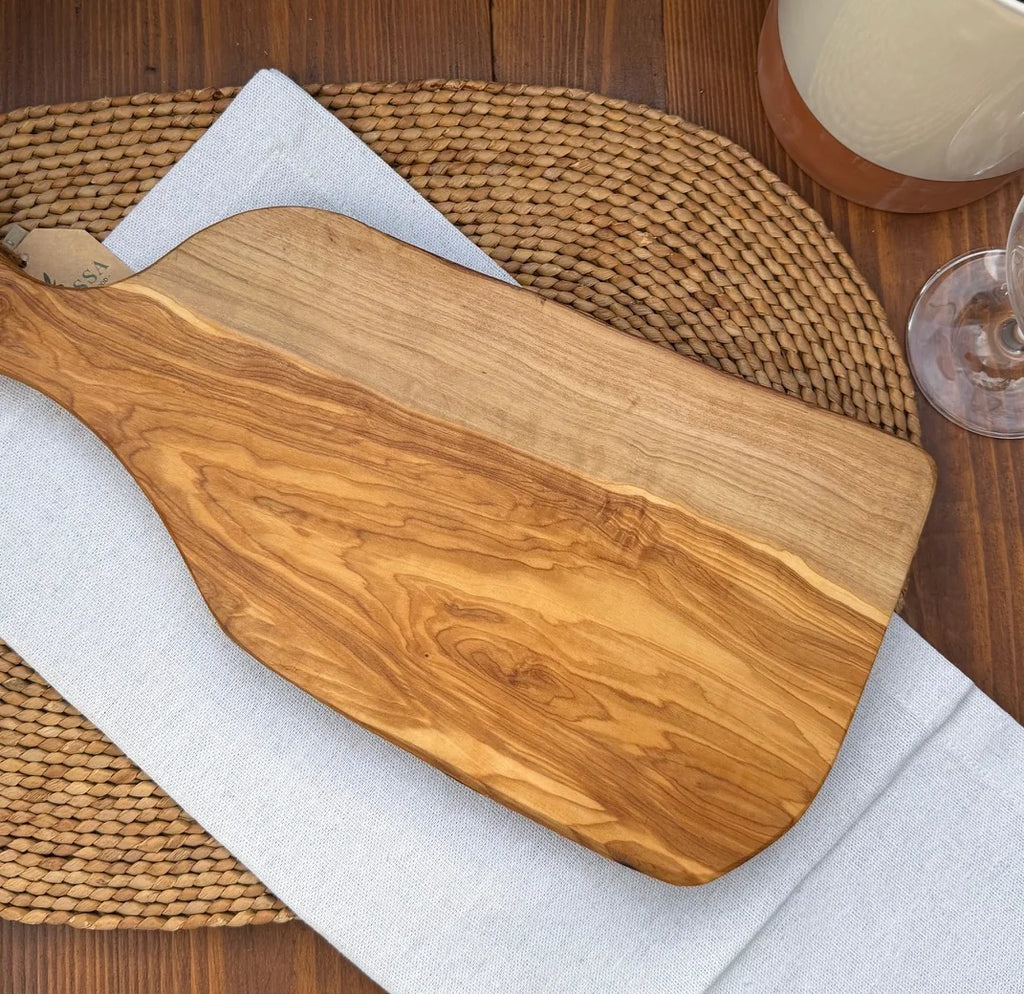 Rustic live-edge olive wood serving board styled on a white napkin over a woven placemat.