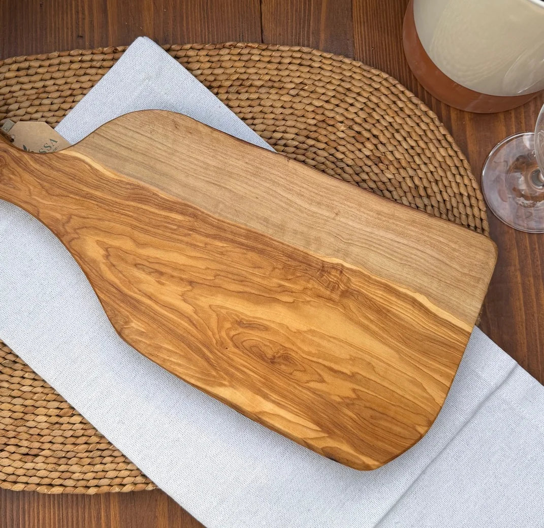 Rustic live-edge olive wood serving board styled on a white napkin over a woven placemat.
