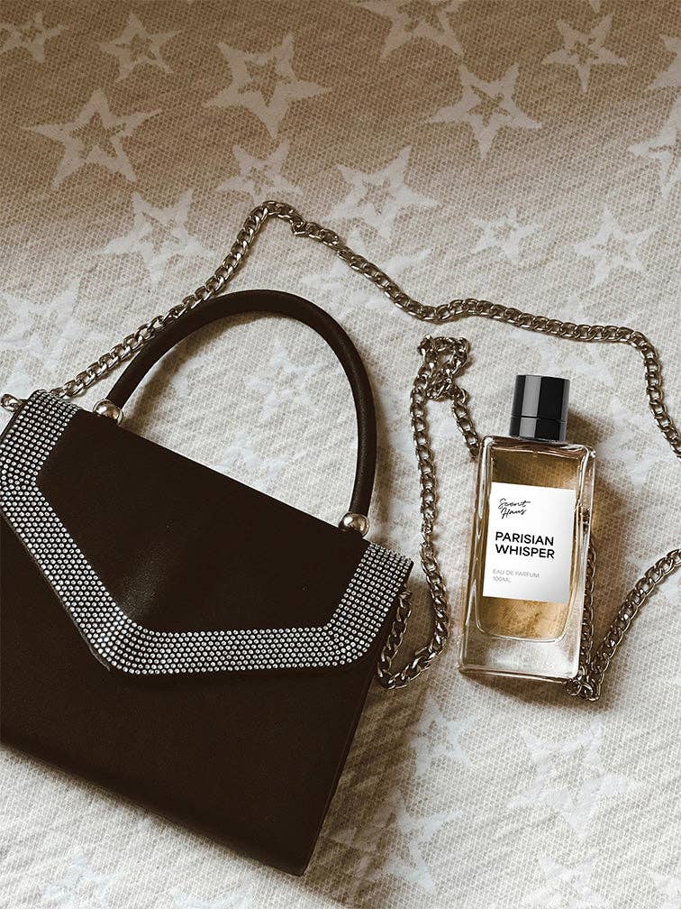 Black handbag with gold chain and 'Parisian Whisper' perfume bottle on textured surface