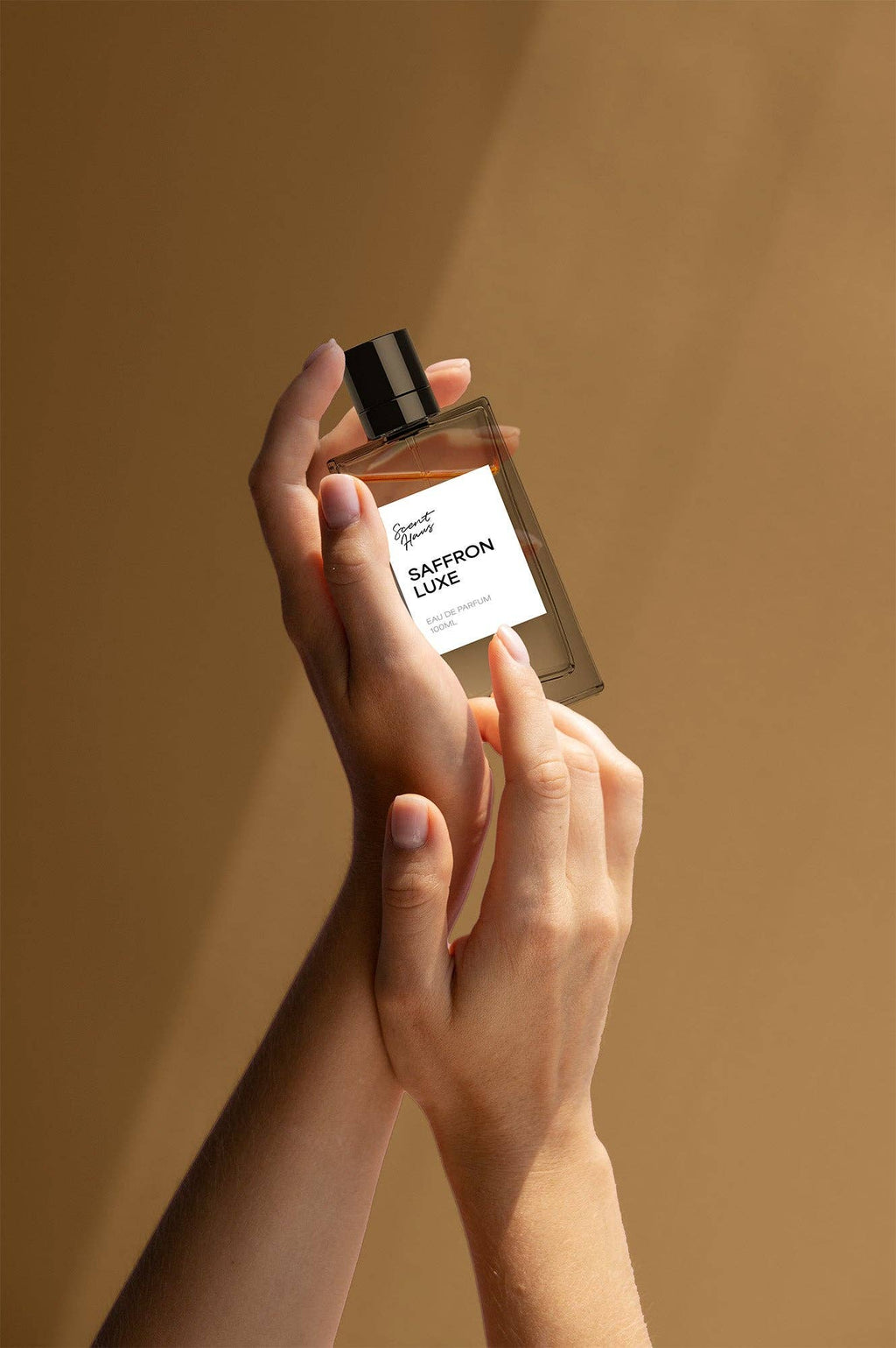 Hand holding a perfume bottle labelled 'Saffron Luxe' against a beige background