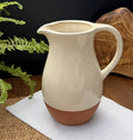 Sintra terracotta ceramic pitcher with a glossy cream glaze and raw brown base styled with fern leaves.