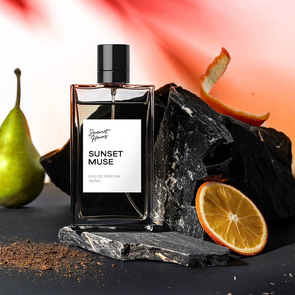 Perfume bottle labeled 'Sunset Muse' with a pear, orange, and rock on a dark surface.