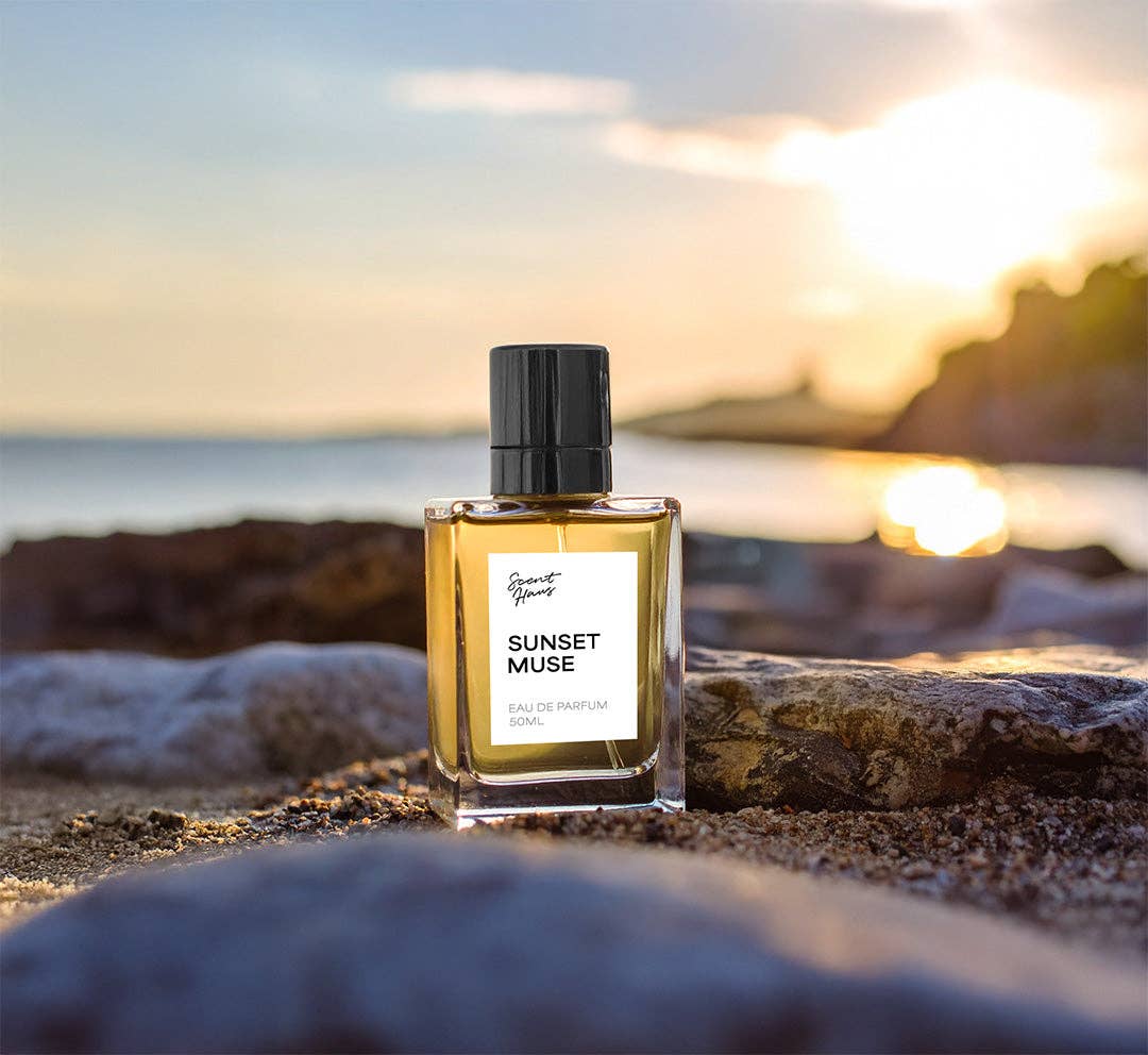 Perfume bottle labeled 'Sunset Muse' on a beach with sunset in the background