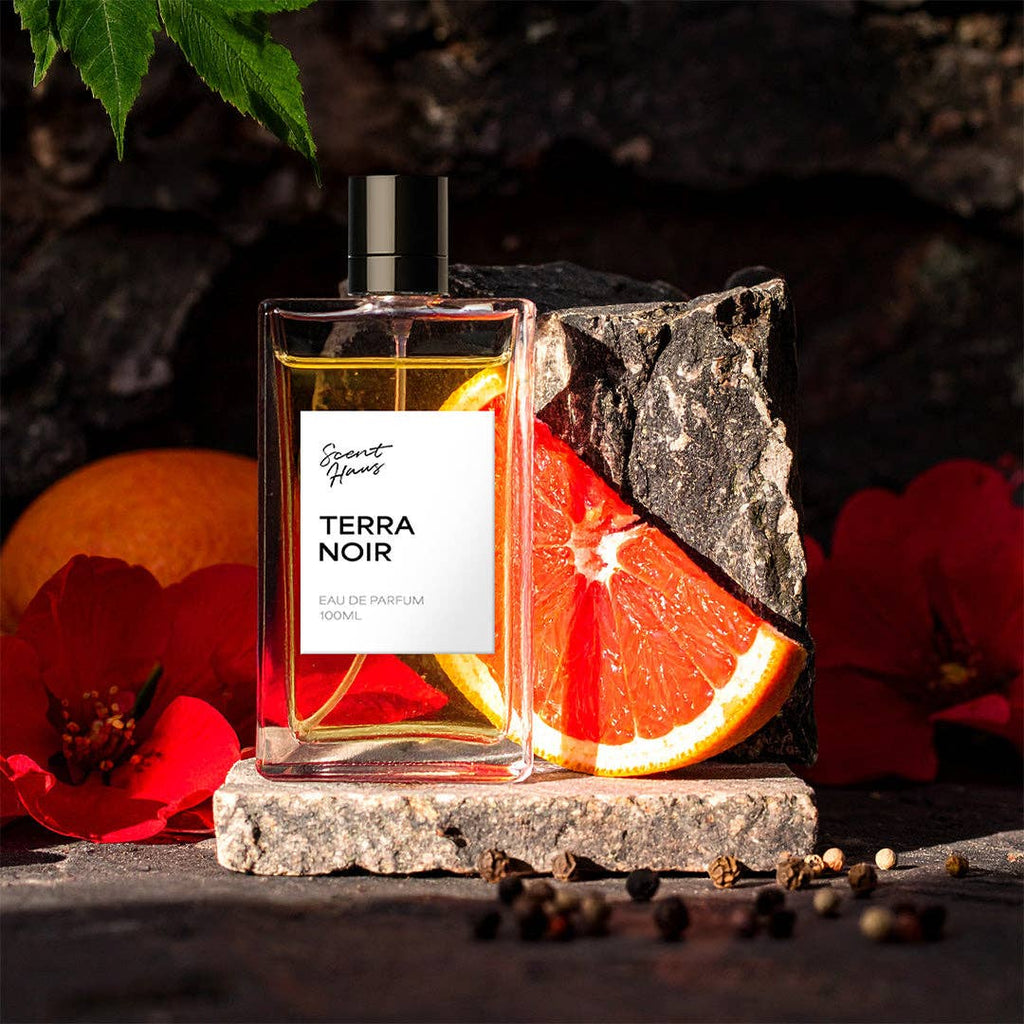 Perfume bottle labeled 'Terra Noir' with a slice of grapefruit and red flowers on a dark background