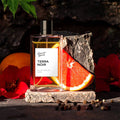 Perfume bottle labeled 'Terra Noir' with a slice of grapefruit and red flowers on a dark background