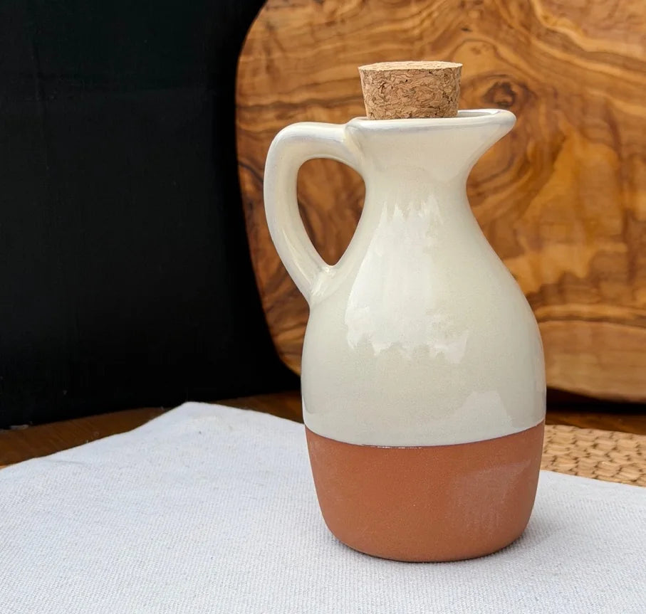 Terracotta oil drizzler with glossy off-white glaze and cork stopper on a white cloth.
