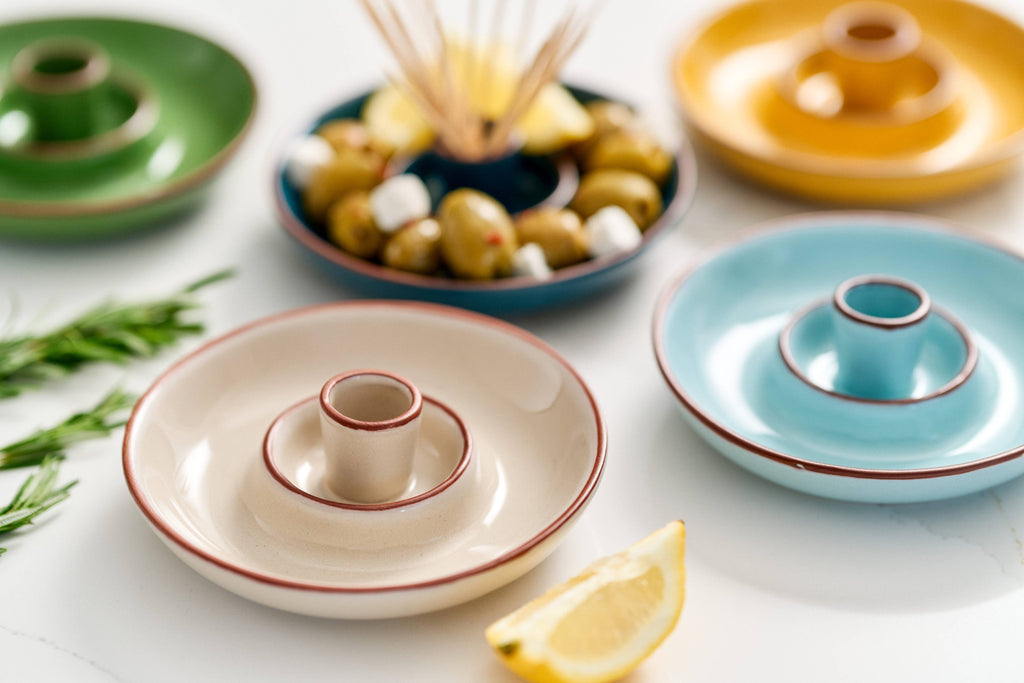 Colourful glazed terracotta olive dishes arranged on a clean white surface.