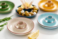 Colourful glazed terracotta olive dishes arranged on a clean white surface.