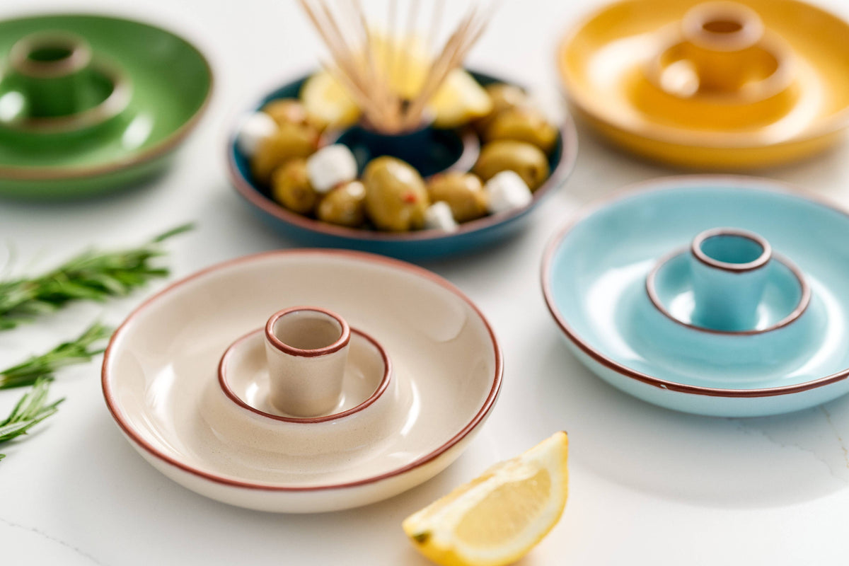 Colourful glazed terracotta olive dishes arranged on a clean white surface.