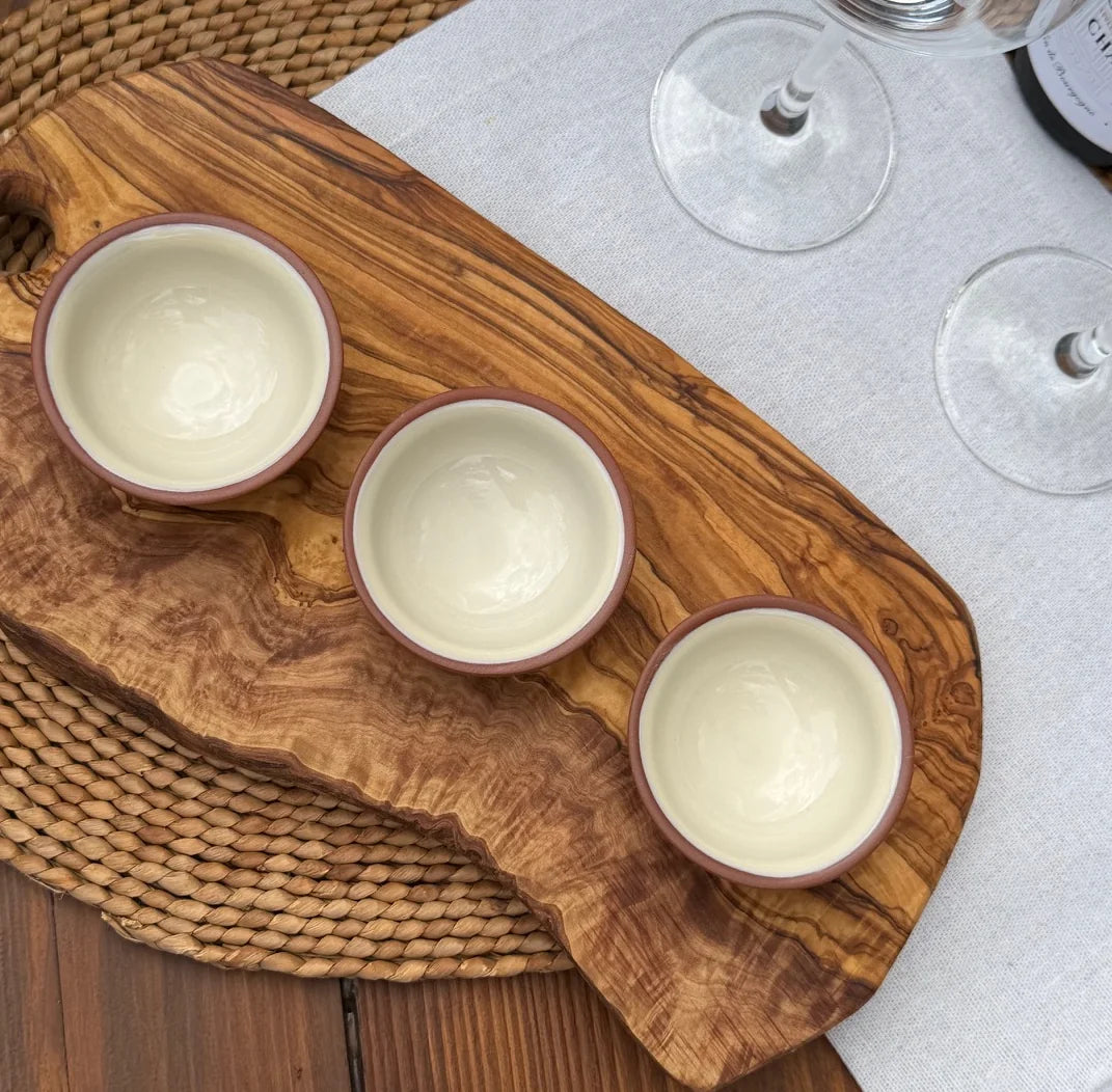 Three terracotta pinch pots with cream interiors arranged on a rustic olive wood board.