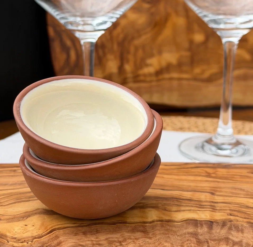 Three stacked terracotta pinch pots with glossy cream interiors on a wooden surface.