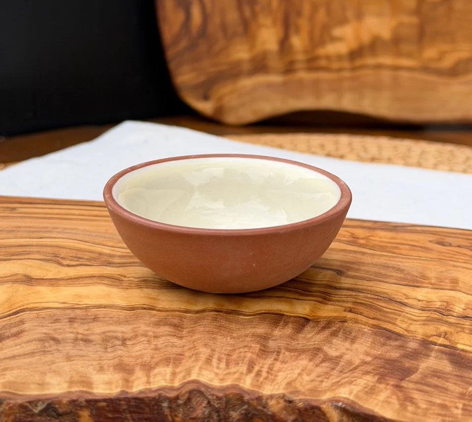 Terracotta pinch pot with glossy cream glaze interior resting on a rustic olive wood slab.