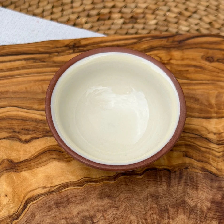 Top-down view of a terracotta pinch pot with glossy off-white interior on a rustic olive wood surface.