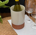 Terracotta wine cooler with glossy cream upper glaze holding a green bottle on a woven placemat.