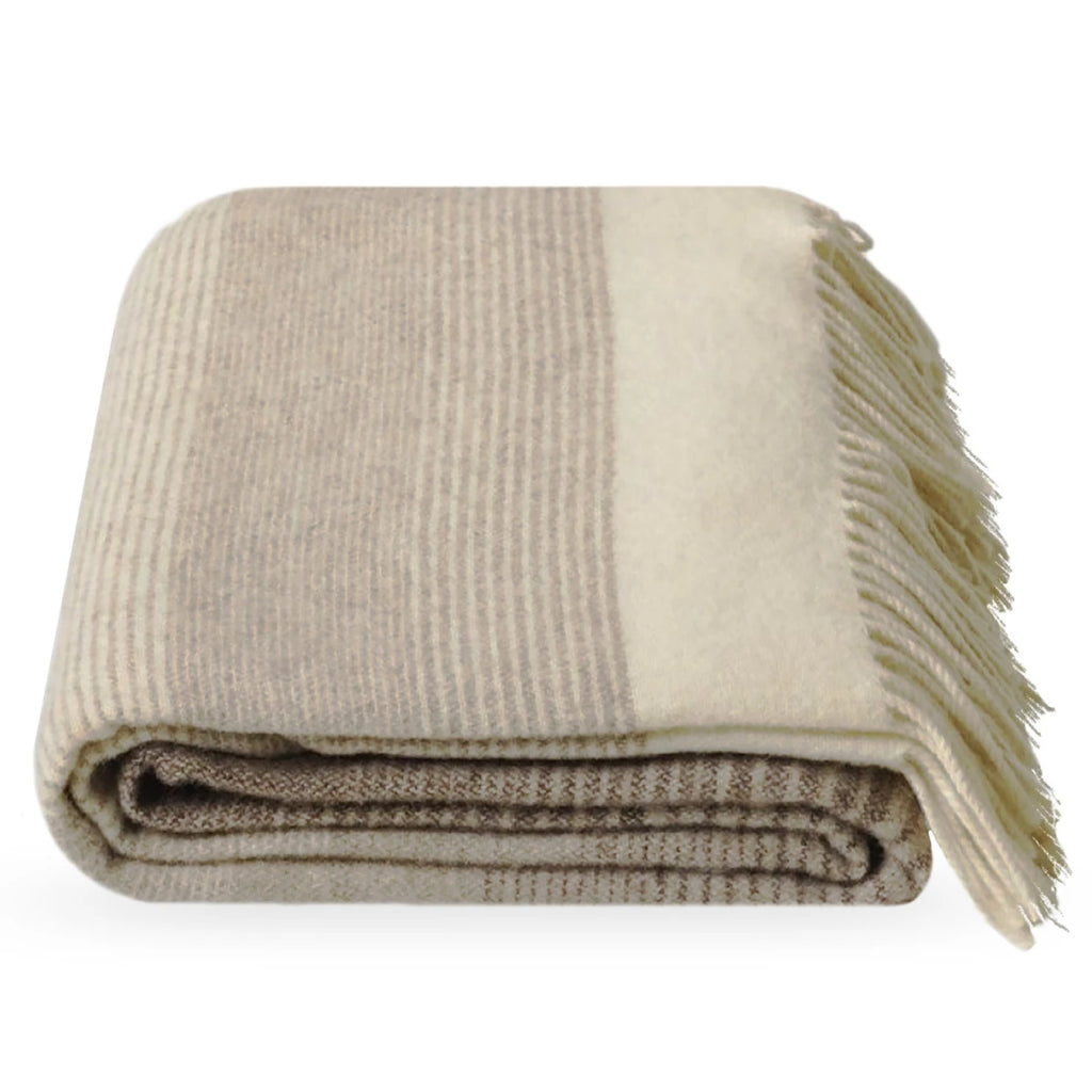 A folded Dolores woollen throw blanket with fringed edges, featuring a striped pattern in beige, taupe, and cream on a white background.