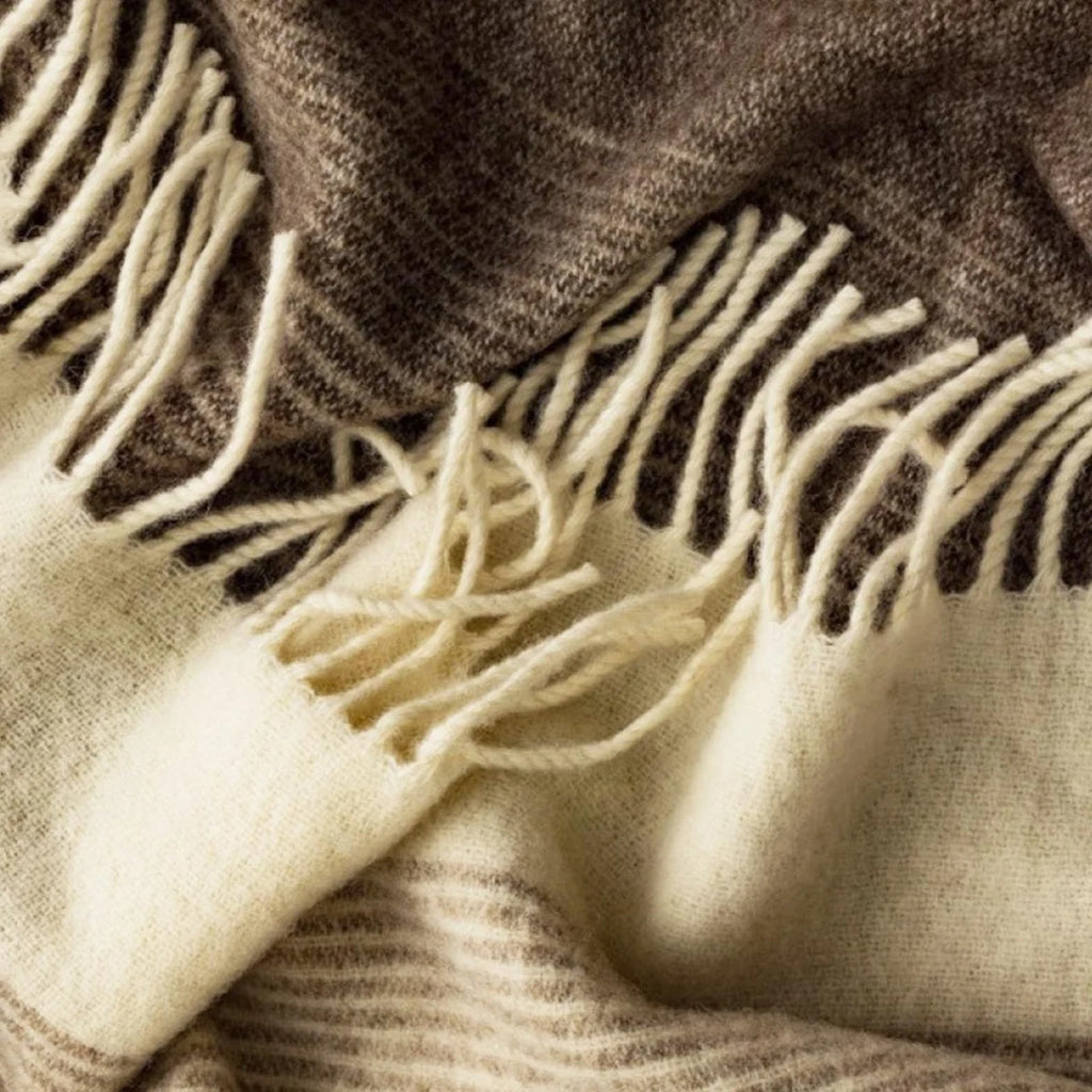 A close-up of a soft woollen Doroles throw with cream fringe and a brown-and-cream striped plaid pattern.
