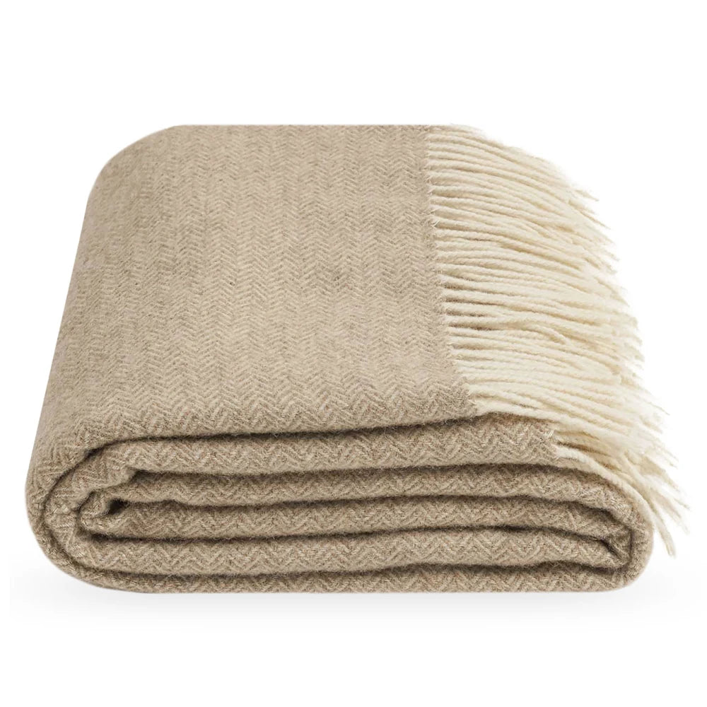 A folded Legenda throw blanket with a herringbone pattern in beige and cream, featuring cream fringe, shown on a plain white background.