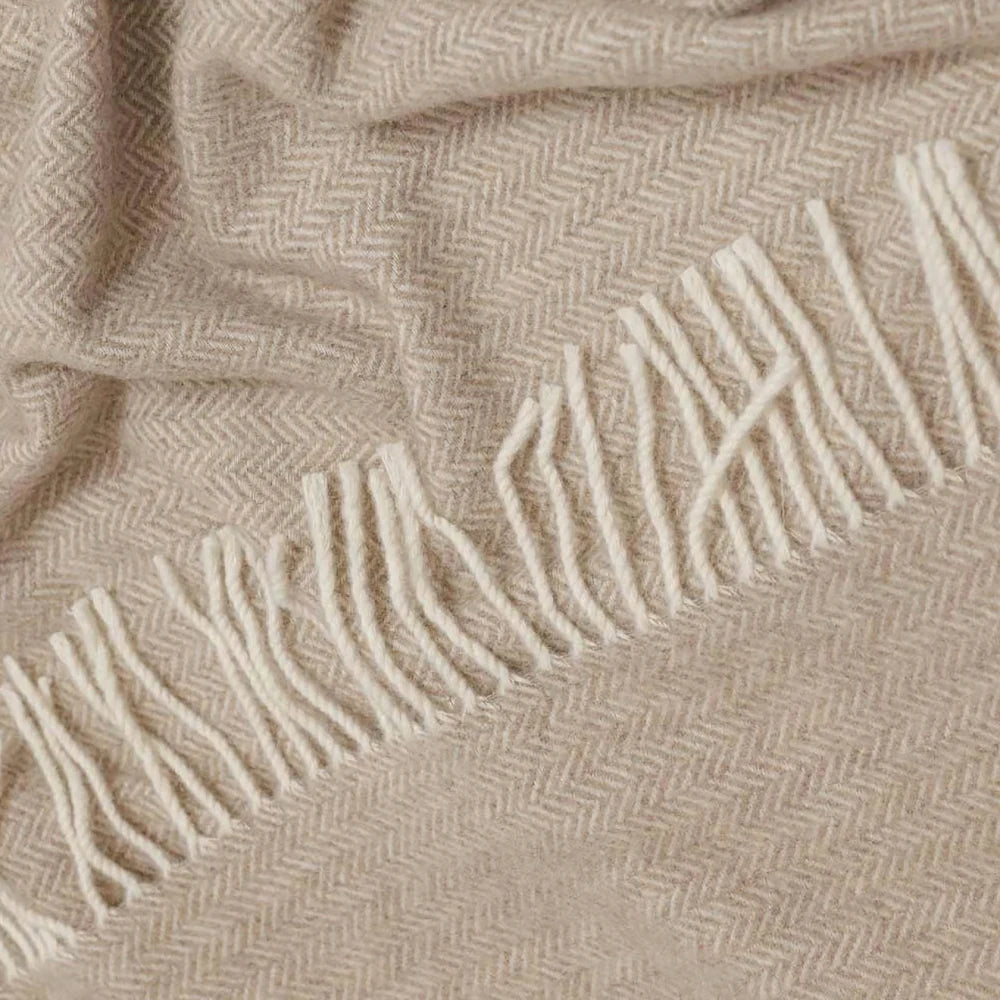 Close-up of a Legenda wool throw with a beige and off-white herringbone pattern and fringed edge.