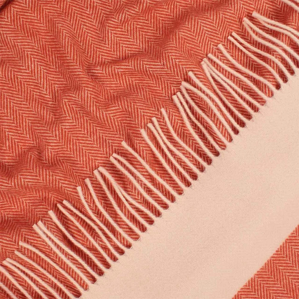 Close-up of a Montre merino wool throw with an orange herringbone pattern, cream fringe, and a solid pale beige border.
