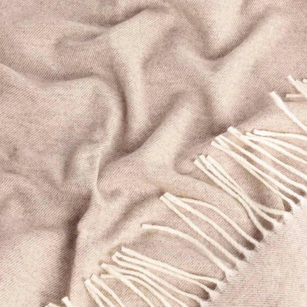 A close-up of a soft Steppe wool throw in a warm light beige tone with white fringe along one edge.