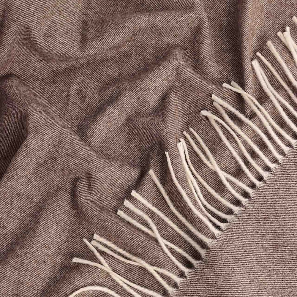 A close-up of a brown Steppe merino wool throw with cream fringe along one edge, showing the fabric texture and draped folds.