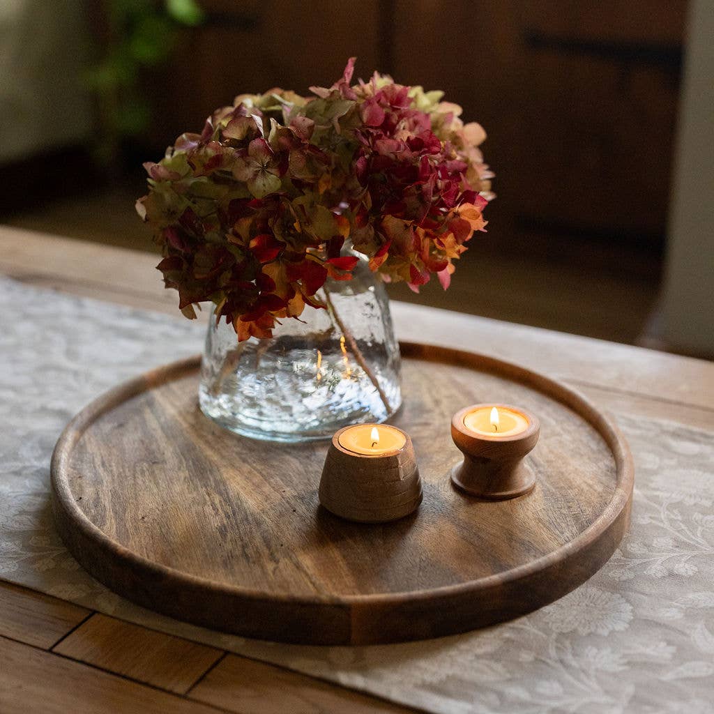 Two wooden tea light holders lit beside dried hydrangeas on a dark wood tray, styled with natural home accessories.