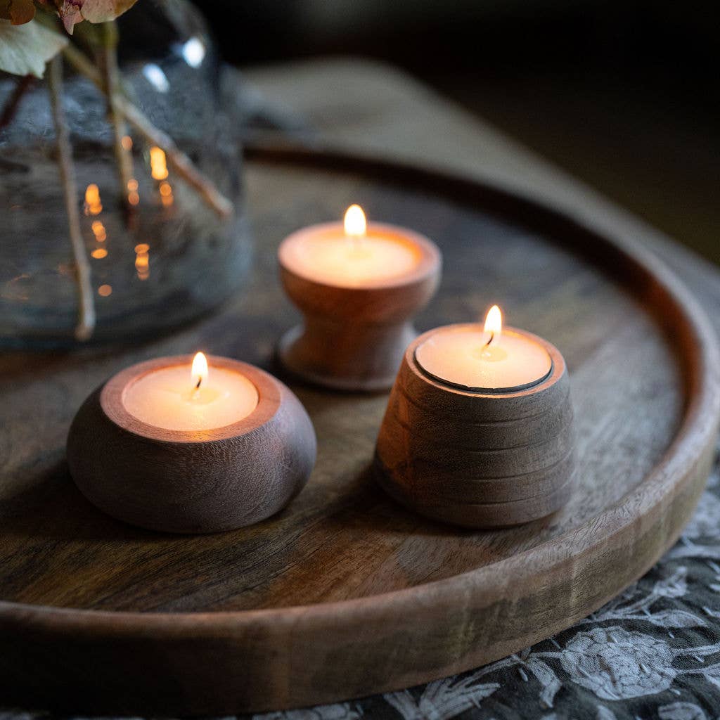 Flickering tealights in small handcrafted acacia wooden candle holders arranged on a decorative tray.