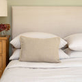 Neatly made bed with beige Westley Bolster linen cushion and white bedding in a bedroom setting.