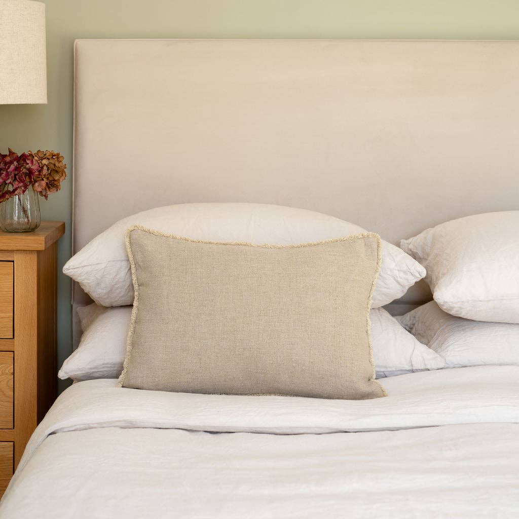 Neatly made bed with beige Westley Bolster linen cushion and white bedding in a bedroom setting.