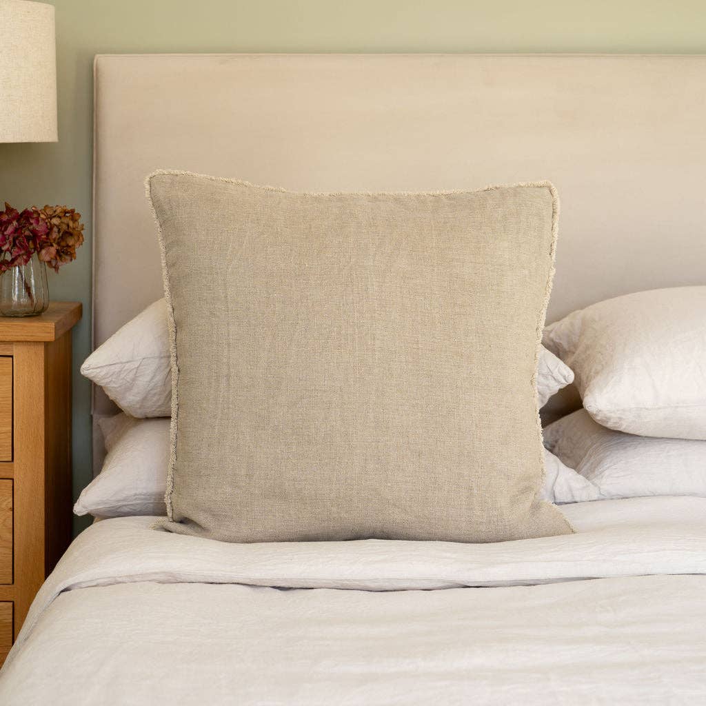Westley square beige linen cushion cover styled on a bed, paired with natural material cushions and white linens.