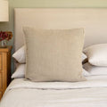 Westley square beige linen cushion cover styled on a bed, paired with natural material cushions and white linens.