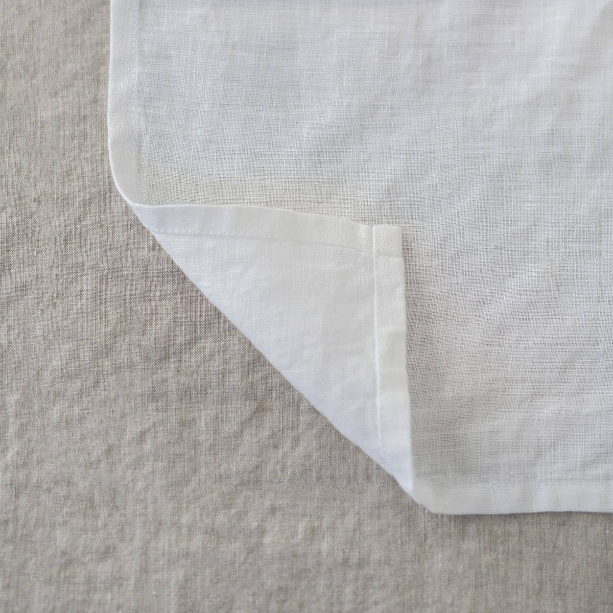 A close-up of the folded corner of a white linen napkin resting on a textured linen tablecloth.