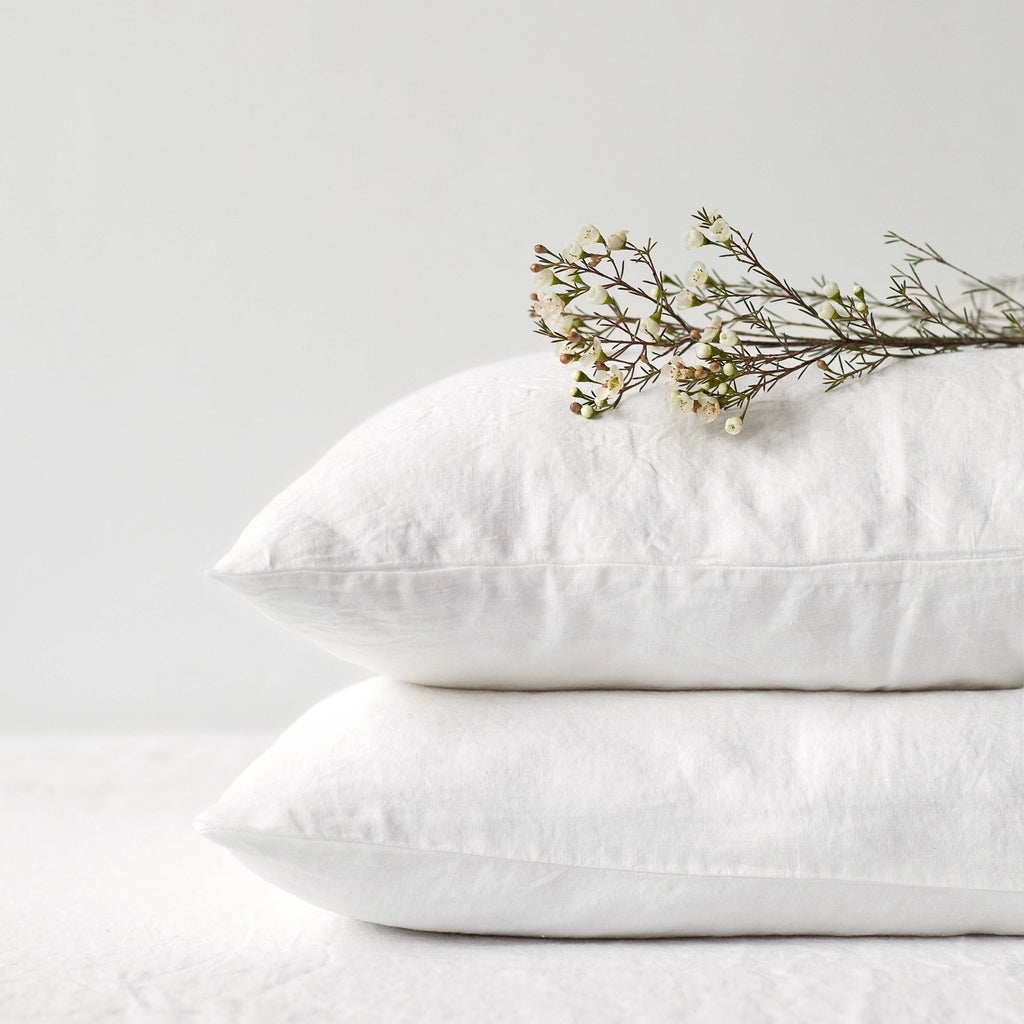 Two stacked white linen pillowcases with delicate white flowers resting on top against a clean background.