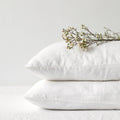 Two stacked white linen pillowcases with delicate white flowers resting on top against a clean background.
