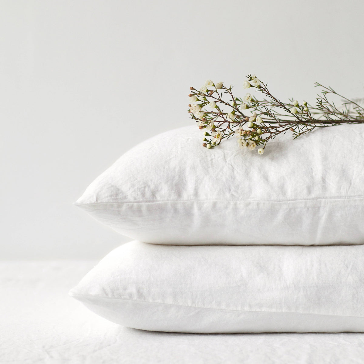 Two stacked white linen pillowcases with delicate white flowers resting on top against a clean background.
