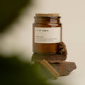 Winter Spice natural scented candle in an amber glass jar with a cork lid on stacked stones with cinnamon sticks.